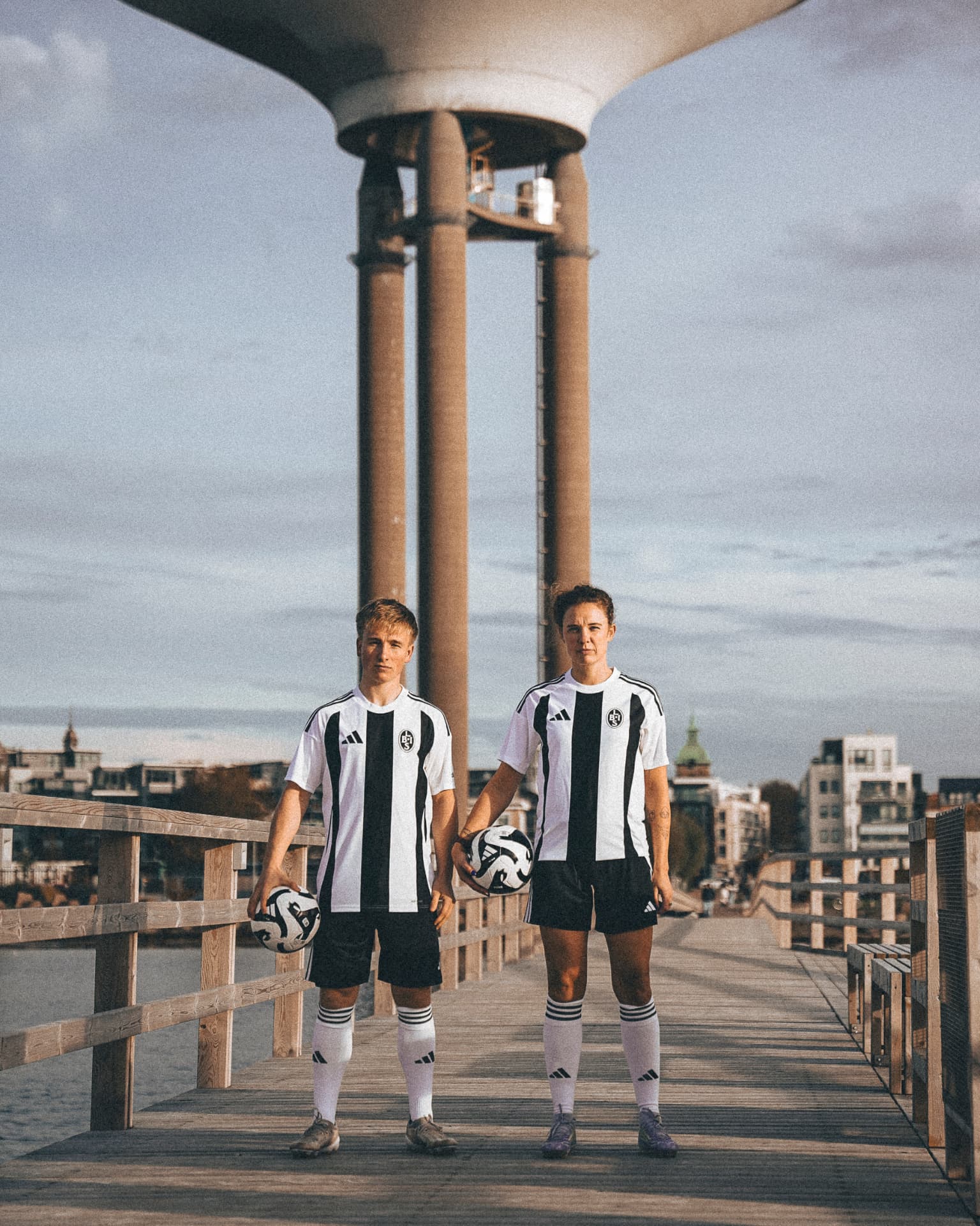 Två fotbollsspelare i randiga tröjor på en brygga framför ett vattentorn