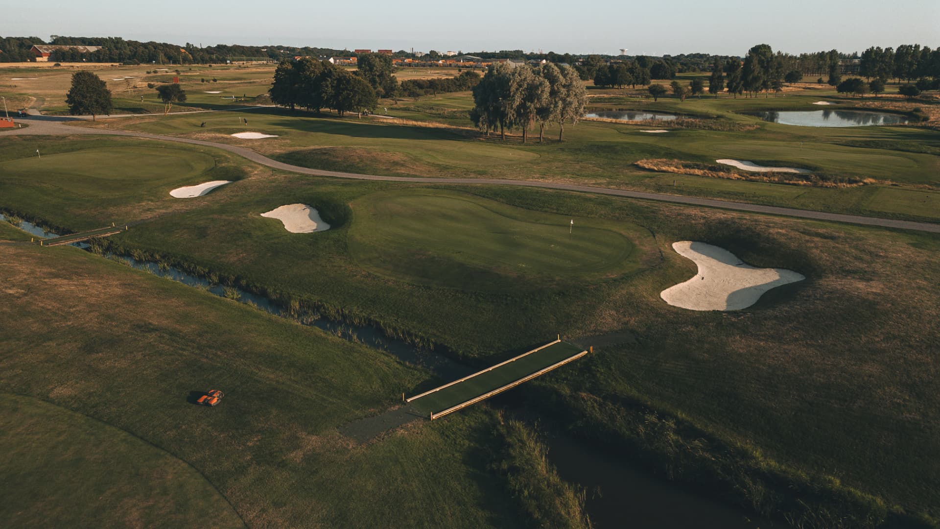 Drönarbild över en golfbana med sandbunkrar och dammar i kvällsljus