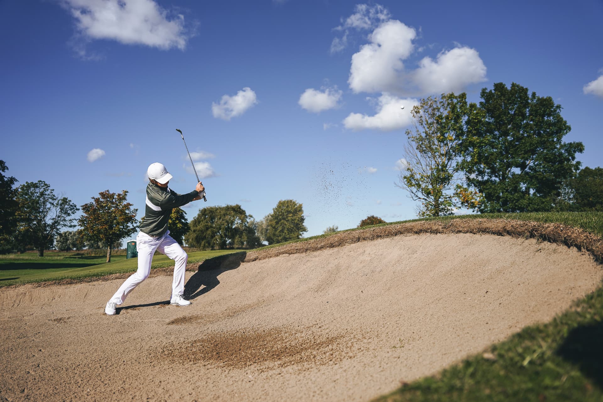 Golfare slår ur en sandbunker under blå himmel